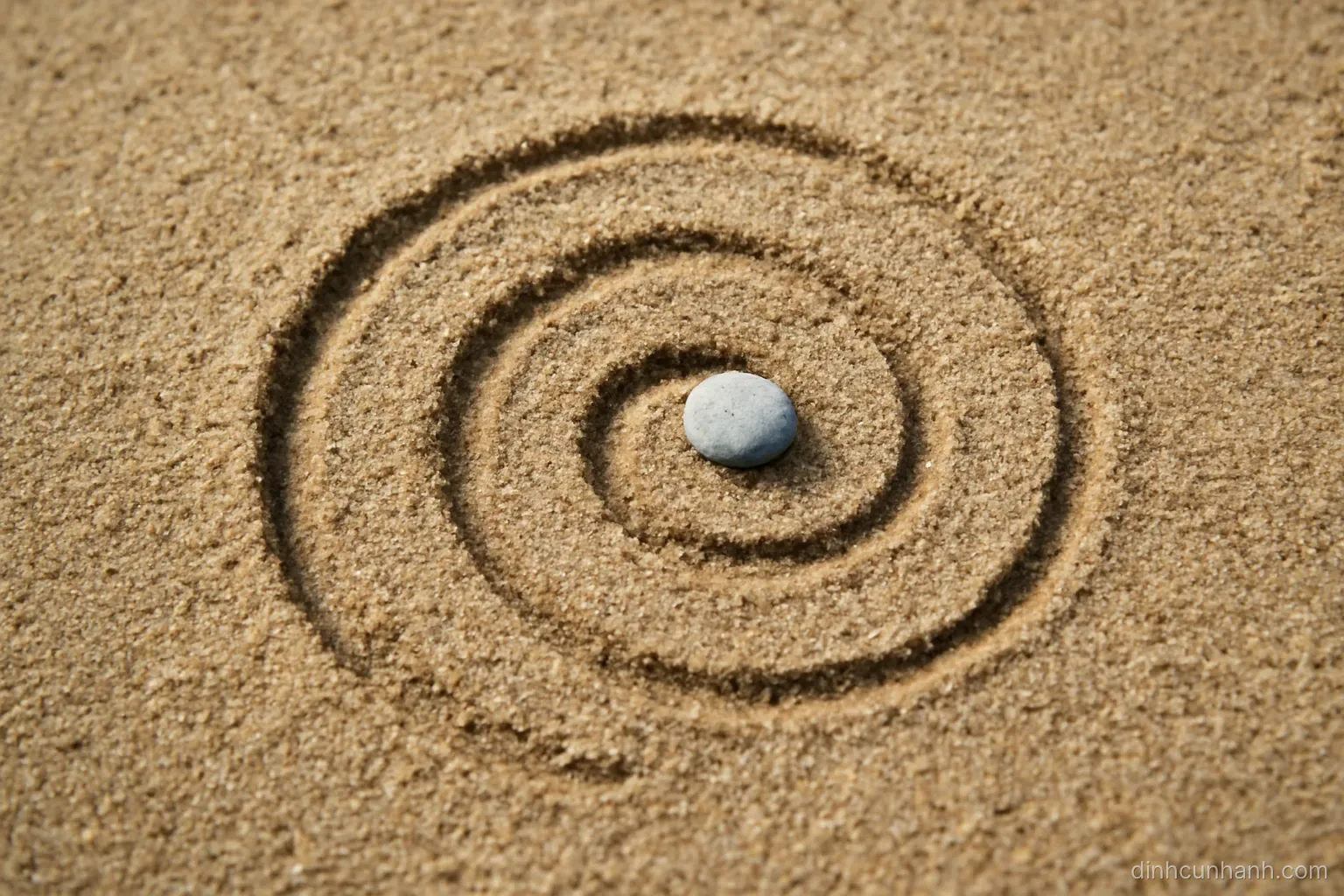 a spiral drawn in sand with a small stone resting in the second turn, seen from directly above